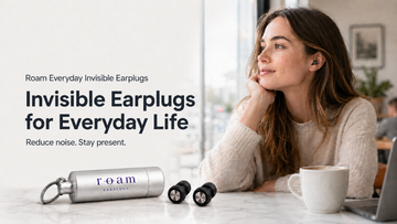 Woman wearing black Roam Everyday Invisible Earplugs in a café with the compact carrying case nearby.