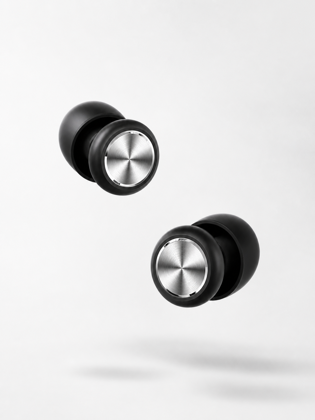 A clean product image showing a pair of black Roam Everyday™ Invisible Earplugs with brushed silver circular faceplates, floating on a soft white background with a subtle shadow.