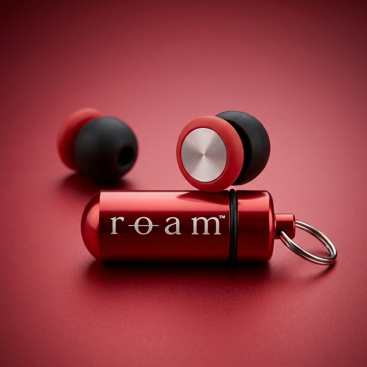 Roam Everyday Invisible Earplugs in Crimson with black silicone tips and a matching Roam Mini Travel Tube in Crimson on a matching red background.